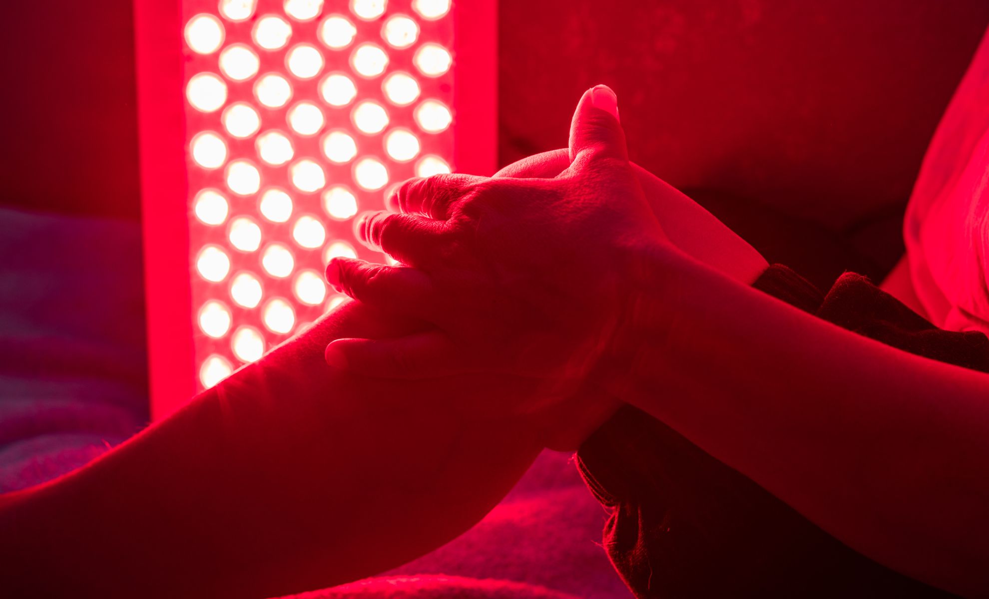 Hands massaging a leg under red light therapy.