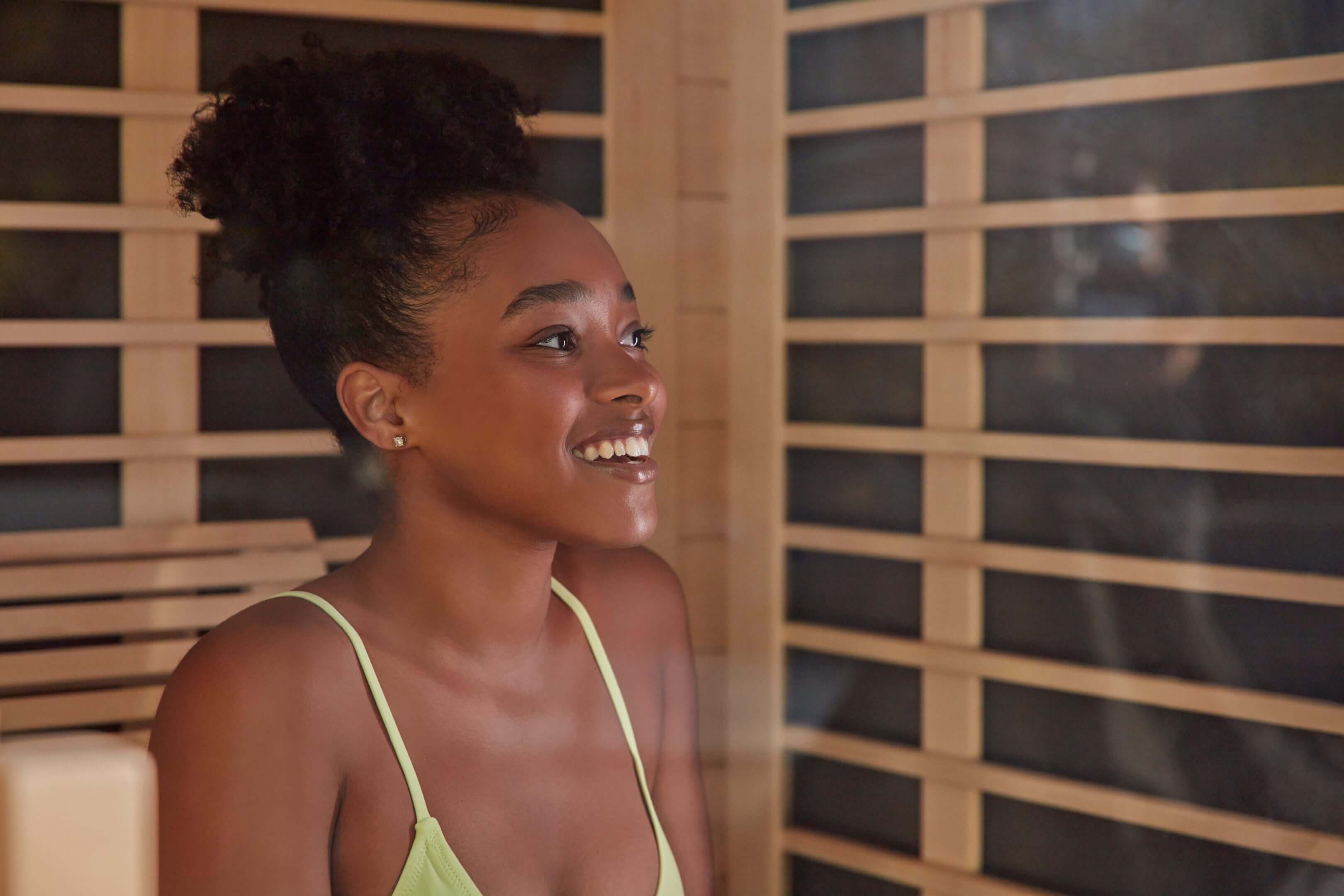 A smiling woman with curly hair in a green top, standing indoors.
